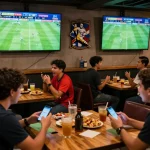 Penggemar yang terlibat merayakan pembaruan Skor Langsung di bar olahraga yang ramai selama pertandingan.